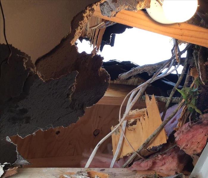 A hole in the roof of a home with wires and wood hanging down from it