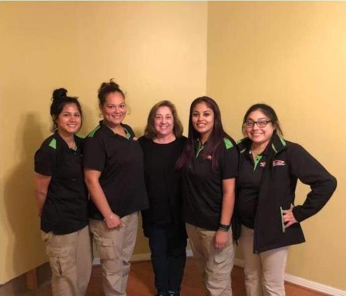 5 women in black shirts and cargo pants smiling side by side for a picture.