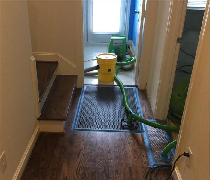 A hallway with wood floor and a green SERVPRO fan drying the floor with tubes coming out of it