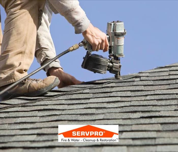 a closeup photo of a roof with a man using a tool on it and the SERVPRO logo in the middle 