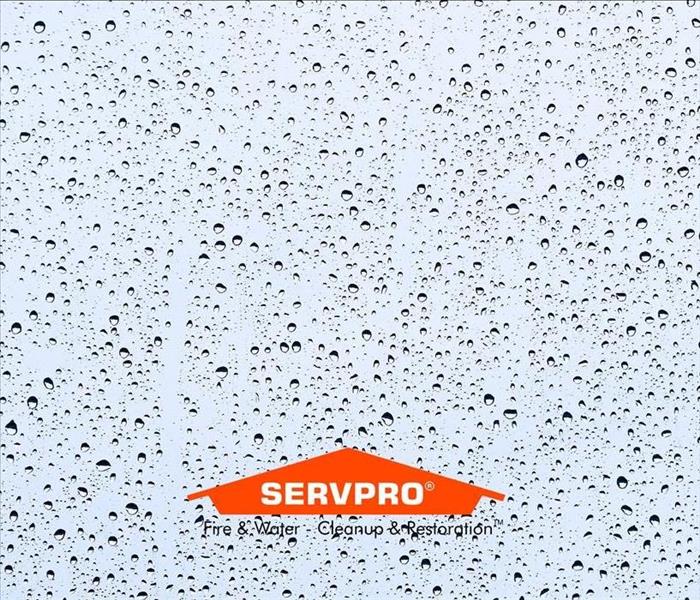 A window with the blue sky and rain drops on it and the SERVPRO logo bottom center