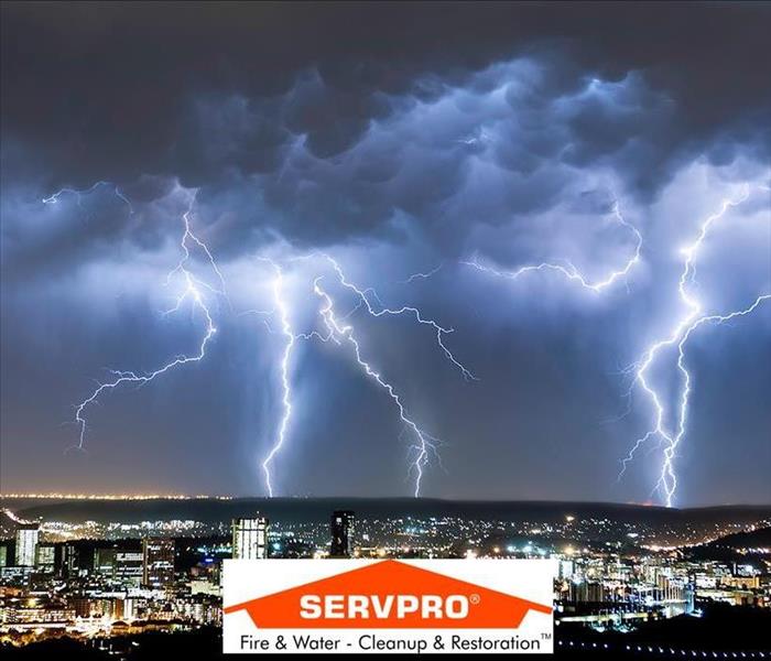 a photo of lightning striking the sky with clouds and a city right below it and the SERVPRO logo in the middle 