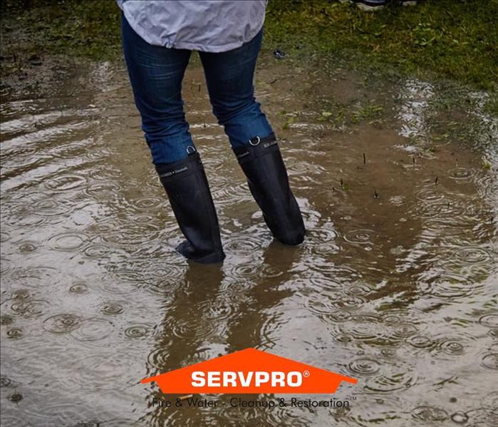 A person in jeans standing in water and the SERVPRO logo 