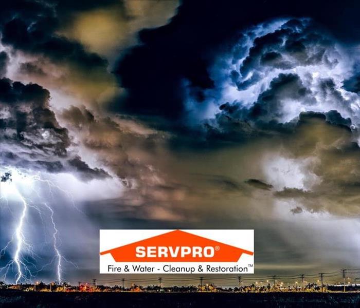 A sky full of blue and white clouds and lightning and a city below and SERVPRO logo